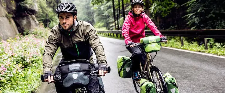 Un homme et une femme font du cyclotourisme avec un vélo électrique chargé de sacoches Ortlieb