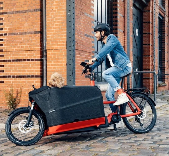 Homme qui transporte un chien dans un vélo cargo électrique Riese & Müller rouge